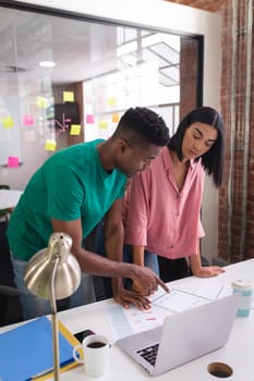 Diverse creative colleagues standing and brainstorming looking at documents in meeting room. independent creative design business.