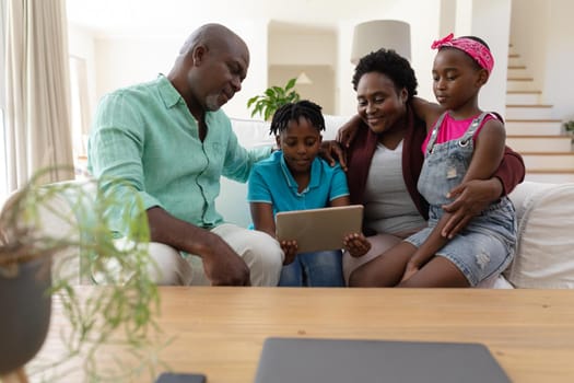 Happy african american grandfather and grandmother on couch with grandchildren looking at tablet. happy family spending time together at home.