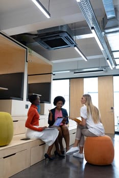 Diverse group of female business colleagues in discussion holding documents using tablet and laptop. business person in a modern office.