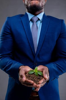 Mid section of african american businessman holding a seedling against grey background. business growth and investment concept