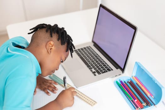 African american boy at desk using laptop with copy space for online school lesson. staying at home in isolation during quarantine lockdown.