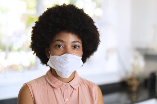 Portrait of african american woman wearing face mask and looking at camera. staying at home in isolation during quarantine lockdown.