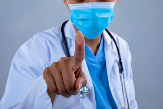 Mid section of doctor wearing face mask touching invisible screen against grey background. business, professionalism and technology concept