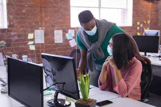 Diverse business colleagues wearing face masks brainstorming in front of computer. independent creative design business during covid 19 coronavirus pandemic.