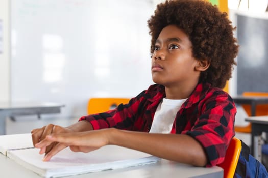 Blind african american schoolboy sitting at desk in classroom reading braille book with fingers. childhood and education at elementary school.