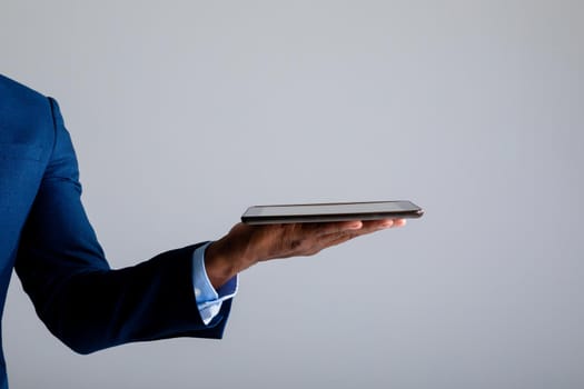 Mid section of african american businessman holding digital tablet against grey background. business, professionalism and technology concept