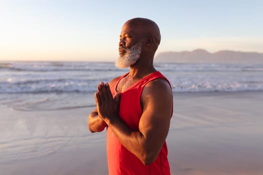 Senior african american man with folded hands meditating and practicing yoga at the beach. fitness yoga and healthy lifestyle concept