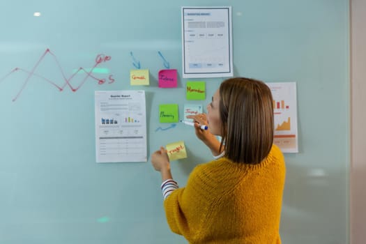 Asian businesswoman standing in front of whiteboard writing and placing memo notes. independent creative design business.