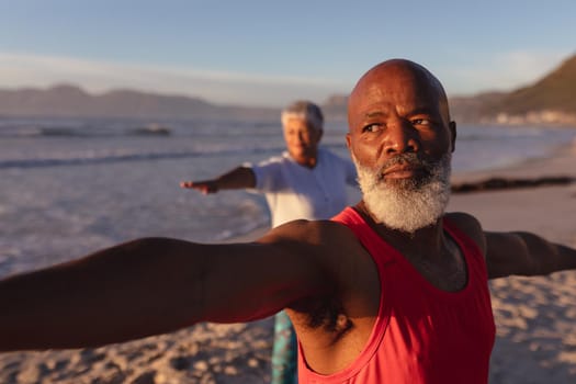 Senior african american couple performing stretching exercise together at the beach. fitness yoga and healthy lifestyle concept