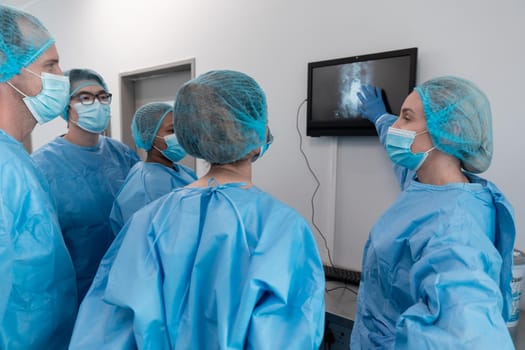 Diverse group of male and female surgeons in operating theatre wearing face masks looking at screen. medicine, health and healthcare services during coronavirus covid 19 pandemic.