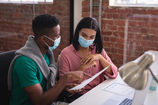 Diverse creative colleagues wearing face masks brainstorming in meeting room. independent creative design business during covid 19 coronavirus pandemic.