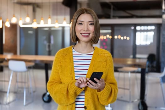 Portrait of asian smiling businesswoman standing holding and using a smartphone. independent creative design business.
