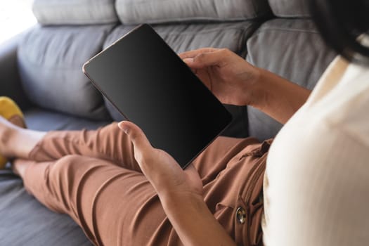 Mixed race gender fluid man relaxing at home on couch using tablet, with copy space screen. staying at home in isolation during quarantine lockdown.