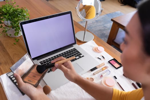 Mixed race gender fluid man using makeup making vlog with laptop, copy space screen. staying at home in isolation during quarantine lockdown.