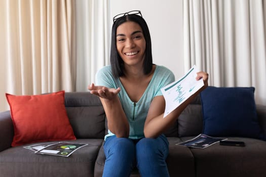 Mixed race gender fluid man working at home making video call holding documents and smiling. staying at home in isolation during quarantine lockdown.