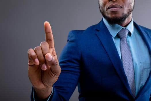 Mid section of african american businessman touching invisible screen against grey background. business, professionalism and technology concept