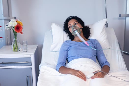 Worried african american female patient in hospital bed with oxygen ventilator. medicine, health and healthcare services during coronavirus covid 19 pandemic.