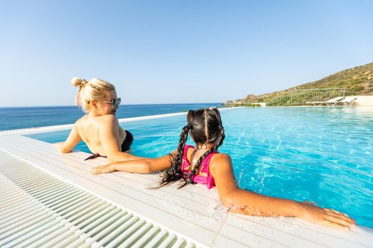 Smiling beautiful woman smears with cream for sunburn little girl near pool in aquapark