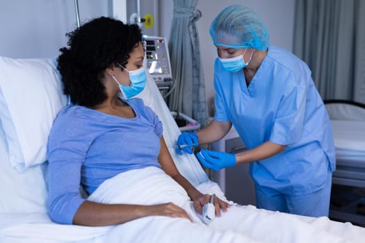 Caucasian female doctor in hospital wearing face mask vaccinating african american female patient. medical professional at work during coronavirus covid 19 pandemic.
