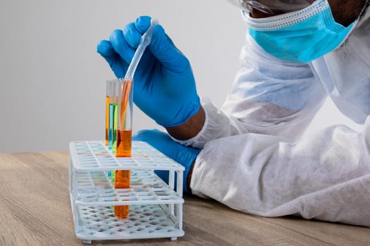 African american male health worker wearing face mask working with chemicals in test tube. medical research and technology concept