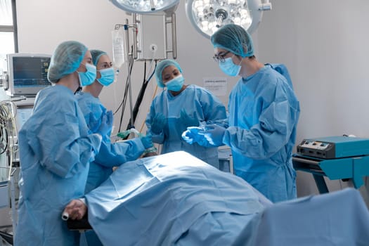 Diverse group of male and female surgeons in operating theatre wearing face masks performing surgery. medicine, health and healthcare services during coronavirus covid 19 pandemic.