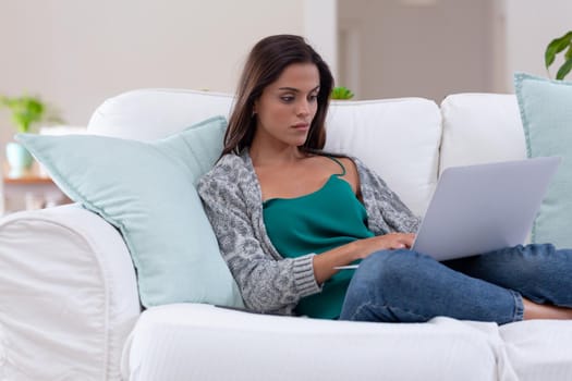 Caucasian woman sitting on a couch using laptop and smiling. staying at home in isolation during quarantine lockdown.