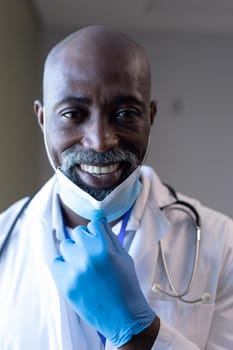 Portrait of smiling african american male doctor in hospital with face mask. medical professional at work during coronavirus covid 19 pandemic.