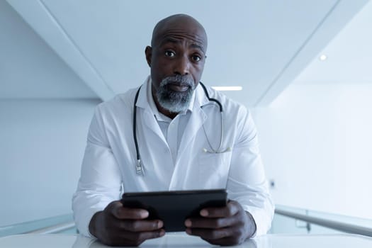 African american male doctor holding tablet sitting at desk giving video call consultation. telemedicine, online healthcare services during quarantine lockdown.