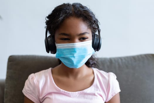 Portrait of mixed race girl wearing face mask and headphones. medicine and health during coronavirus covid 19 pandemic.