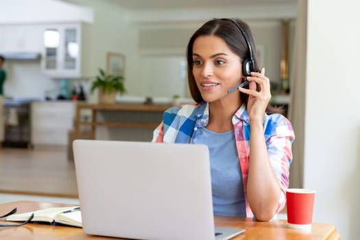 Caucasian woman sitting by desk working from home using laptop and talking on headset. staying at home in isolation during quarantine lockdown.