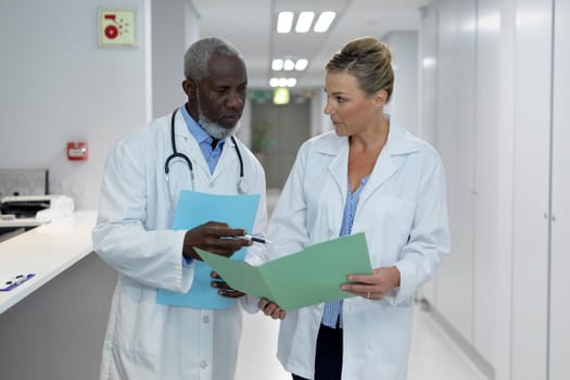 Diverse male and female doctors standing in hospital corridor looking at medical documentation. medicine, health and healthcare services.