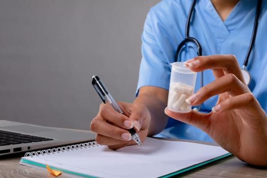 Mid section of female health worker holding medication container and taking notes. healthcare and medical professionalism concept