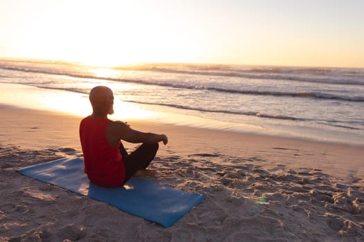 Senior african american man meditating and practicing yoga while sitting on yoga mat at the beach. fitness yoga and healthy lifestyle concept