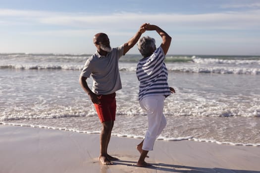 Happy senior african american couple dancing together on the beach. travel vacation retirement lifestyle concept