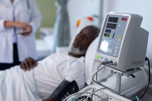 African american male patient lying on hospital bed next to blood pressure monitor. medicine, health and healthcare services.