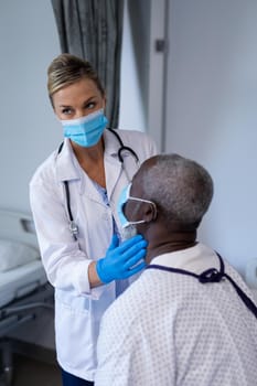 Caucasian female doctor wearing face mask palpating lymph nodes of african american male patient. medicine, health and healthcare services during coronavirus covid 19 pandemic.