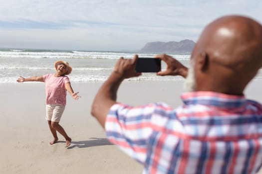 Senior african american man taking a picture of his wife on the beach. travel vacation retirement lifestyle concept