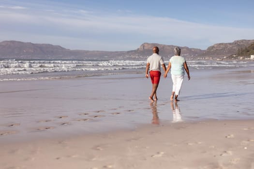 Senior african american couple holding hands while walking on the beach. travel vacation retirement lifestyle concept