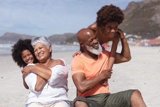 African american grandparents and grandchildren hugging while siting on the beach. travel vacation summer beach concept