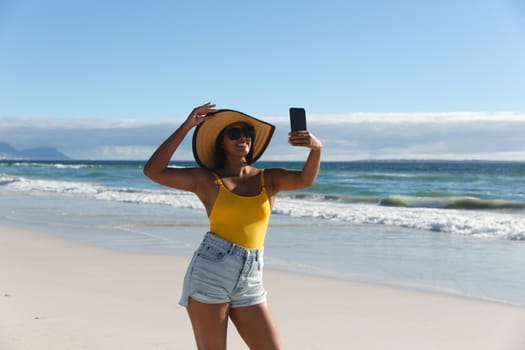 Smiling mixed race woman on beach holiday taking selfie. outdoor leisure vacation time by the sea.