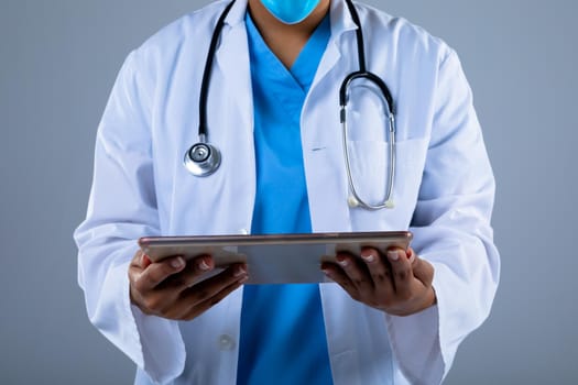 Mid section of female doctor holding digital tablet against grey background. healthcare and medical professionalism concept
