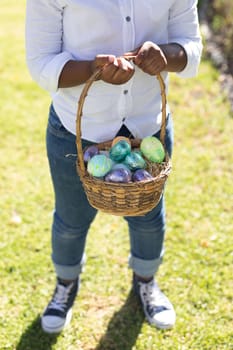 Midsection of african american boy holding basket while easter egg hunting. celebrating easter at home in isolation during quarantine lockdown.