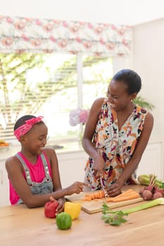 Smiling african american mother teaching daughter cooking in the kitchen. staying at home in isolation during quarantine lockdown.