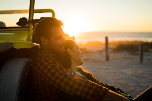 Happy caucasian couple leaning against beach buggy by the sea relaxing during sunset. beach break on summer holiday road trip.