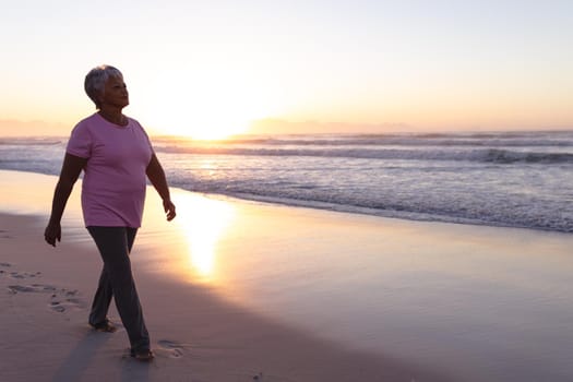 Senior african american woman walking on the beach during sunset. travel vacation retirement lifestyle concept