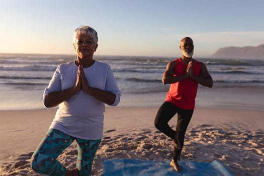 Senior african american couple with folded hands meditating and practicing yoga together at the beach. fitness yoga and healthy lifestyle concept