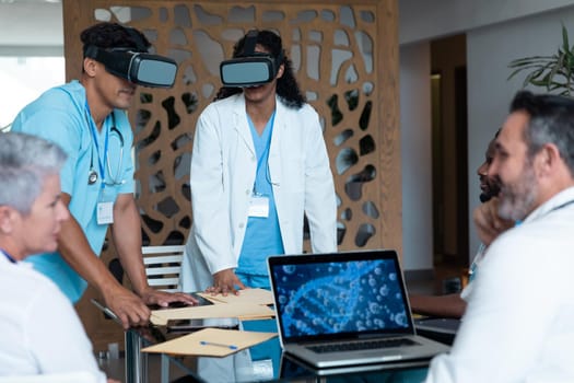 Diverse male and female doctors wearing face masks sitting at table and using vr glasses. medicine, health and healthcare services.