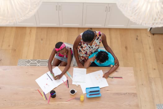 High angle view of african american mother sitting at table with son and daughter doing school work. staying at home in isolation during quarantine lockdown.