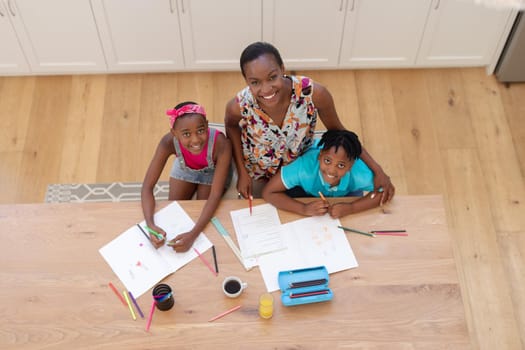 Portrait of smiling african american mother sitting at table with son and daughter doing school work. staying at home in isolation during quarantine lockdown.