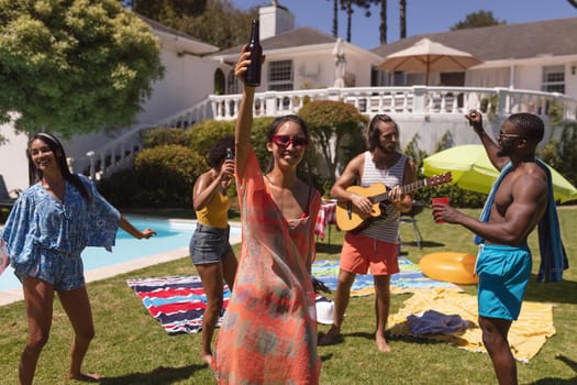 Diverse group of friends having fun at a pool party. hanging out, playing guitar, dancing and relaxing outdoors in summer.